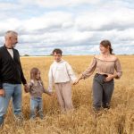 Happy family walking hand in hand through a golden wheat field on a sunny day.